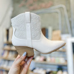 White ankle boot held by a hand with a blurred shoe store background
