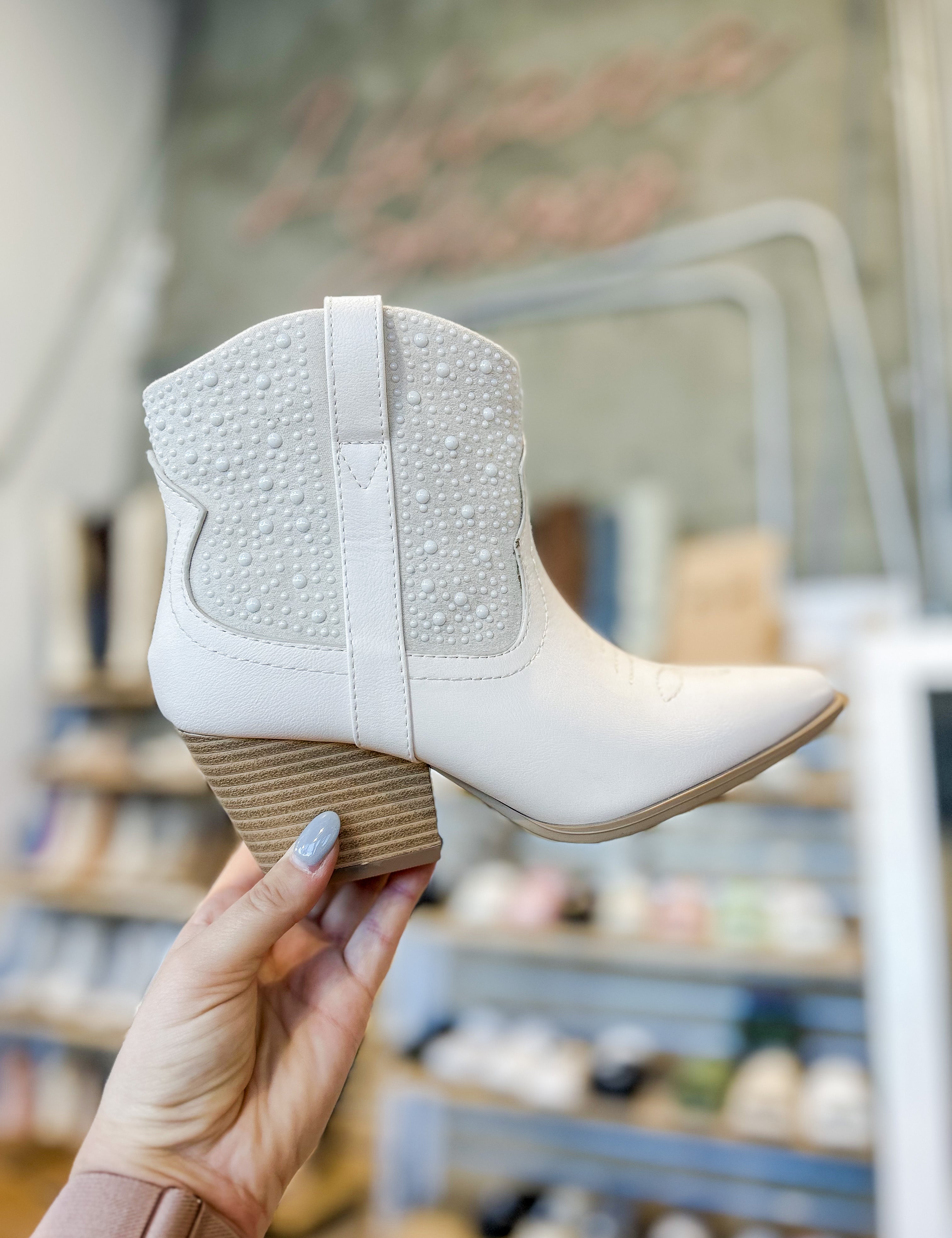 White ankle boot held by a hand with a blurred shoe store background