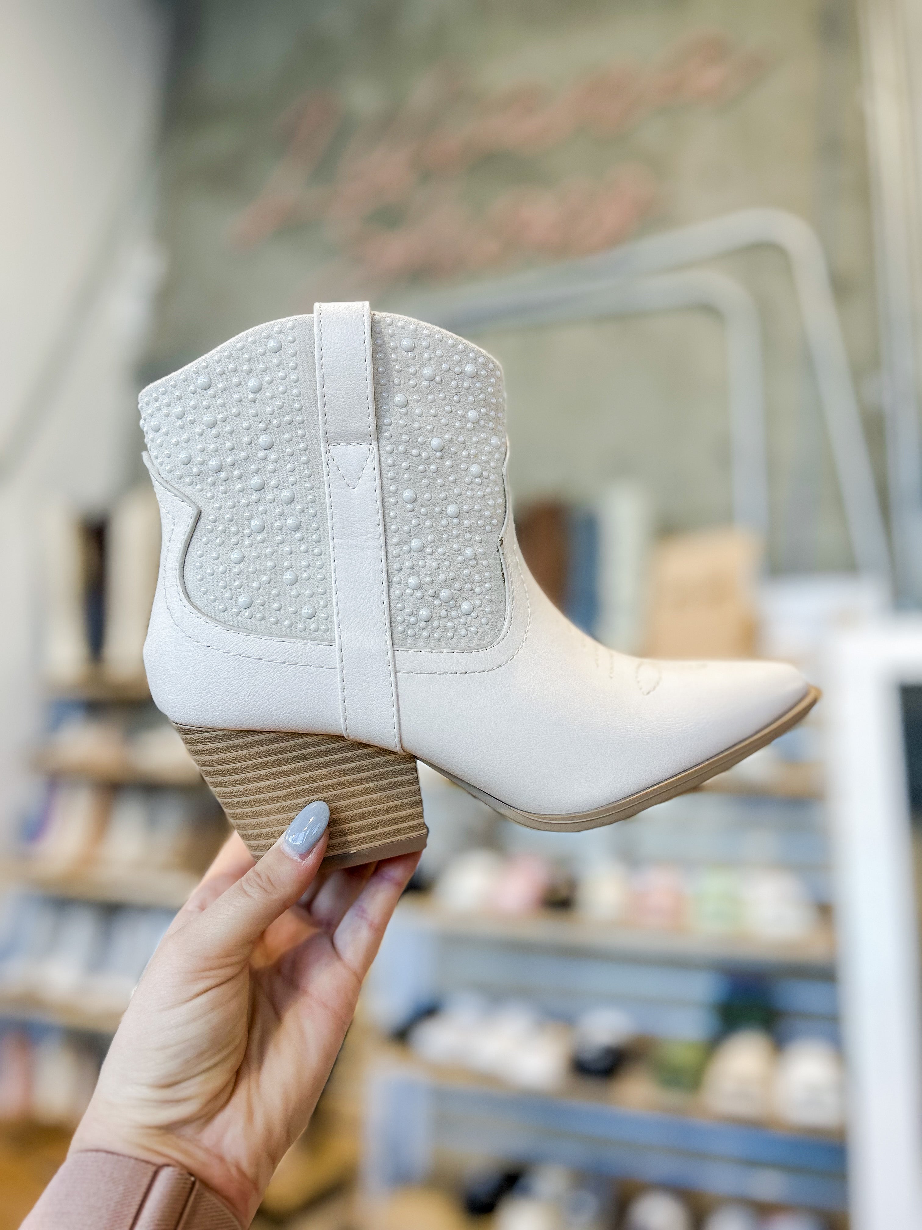 White ankle boot held by a hand with a blurred shoe store background