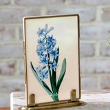 Small brass photo frame with a floral design on a wooden surface.