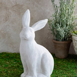 White rabbit statue on grass with a plant in the background