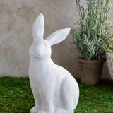 White rabbit statue on grass with a plant in the background