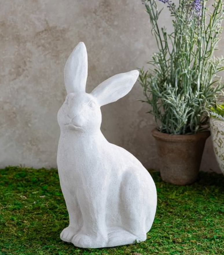 White rabbit statue on grass with a plant in the background