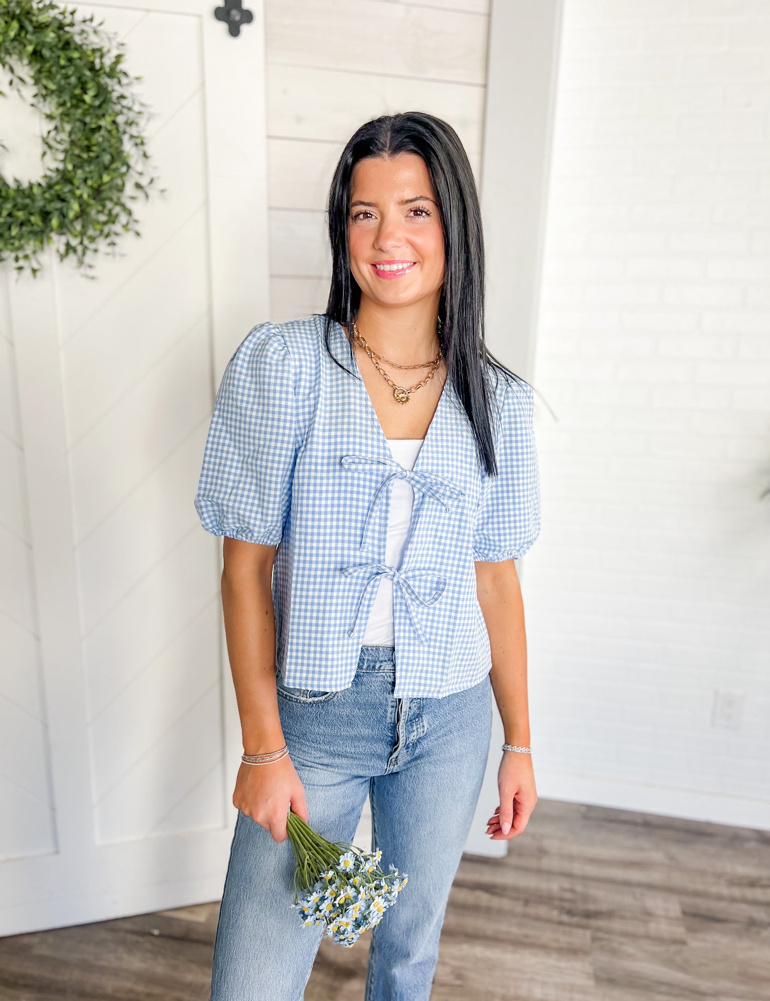 Woman wearing a blue checkered shirt and jeans, holding flowers indoors.